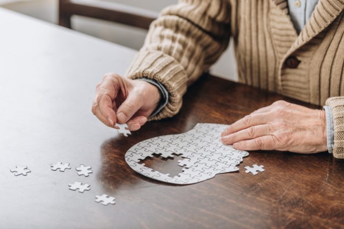 Een oudere man maakt een legpuzzel van een hoofd waarin de stukken van de hersenen nog ontbreken